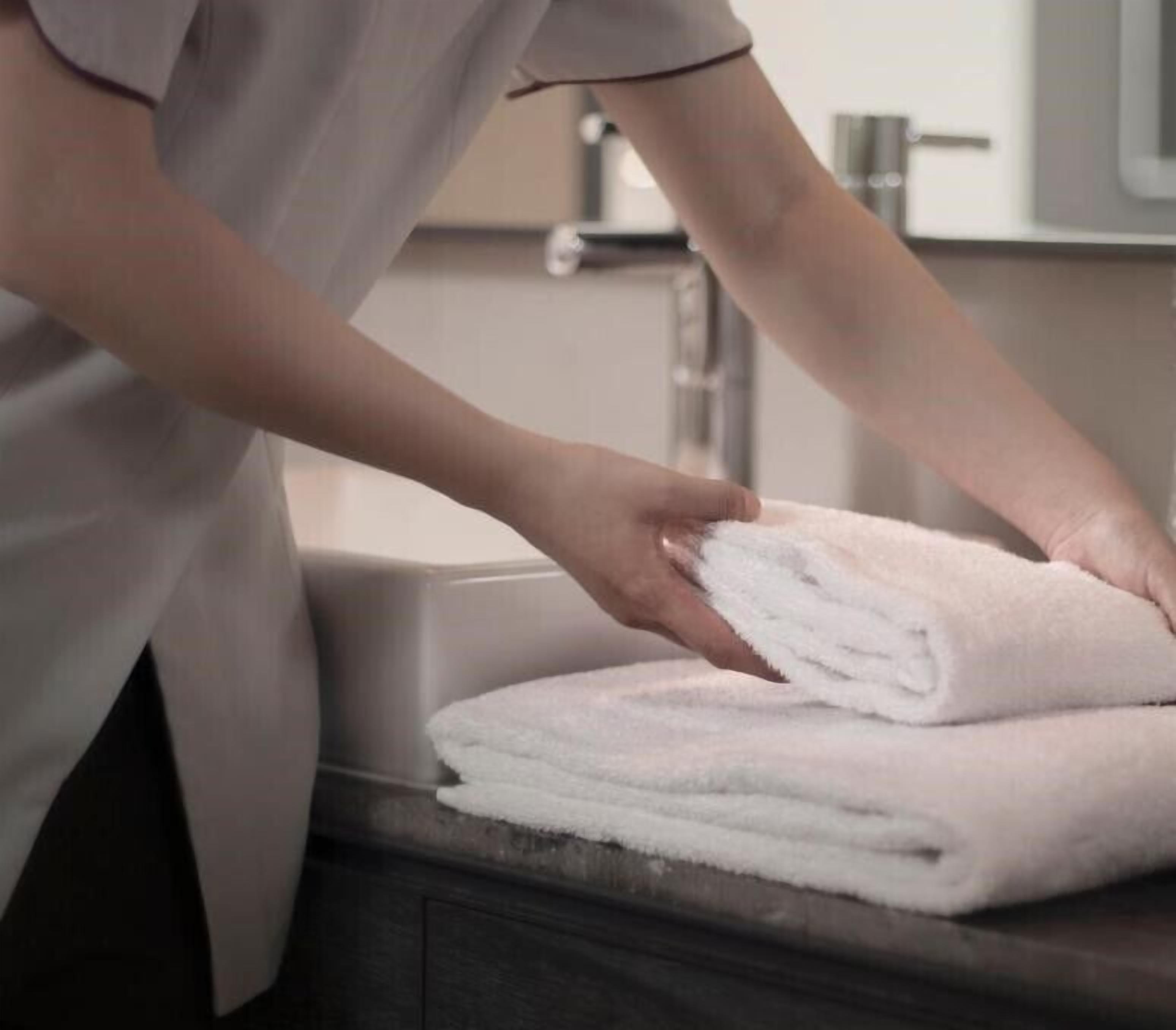 A person folding a white towel on a bathroom counter.