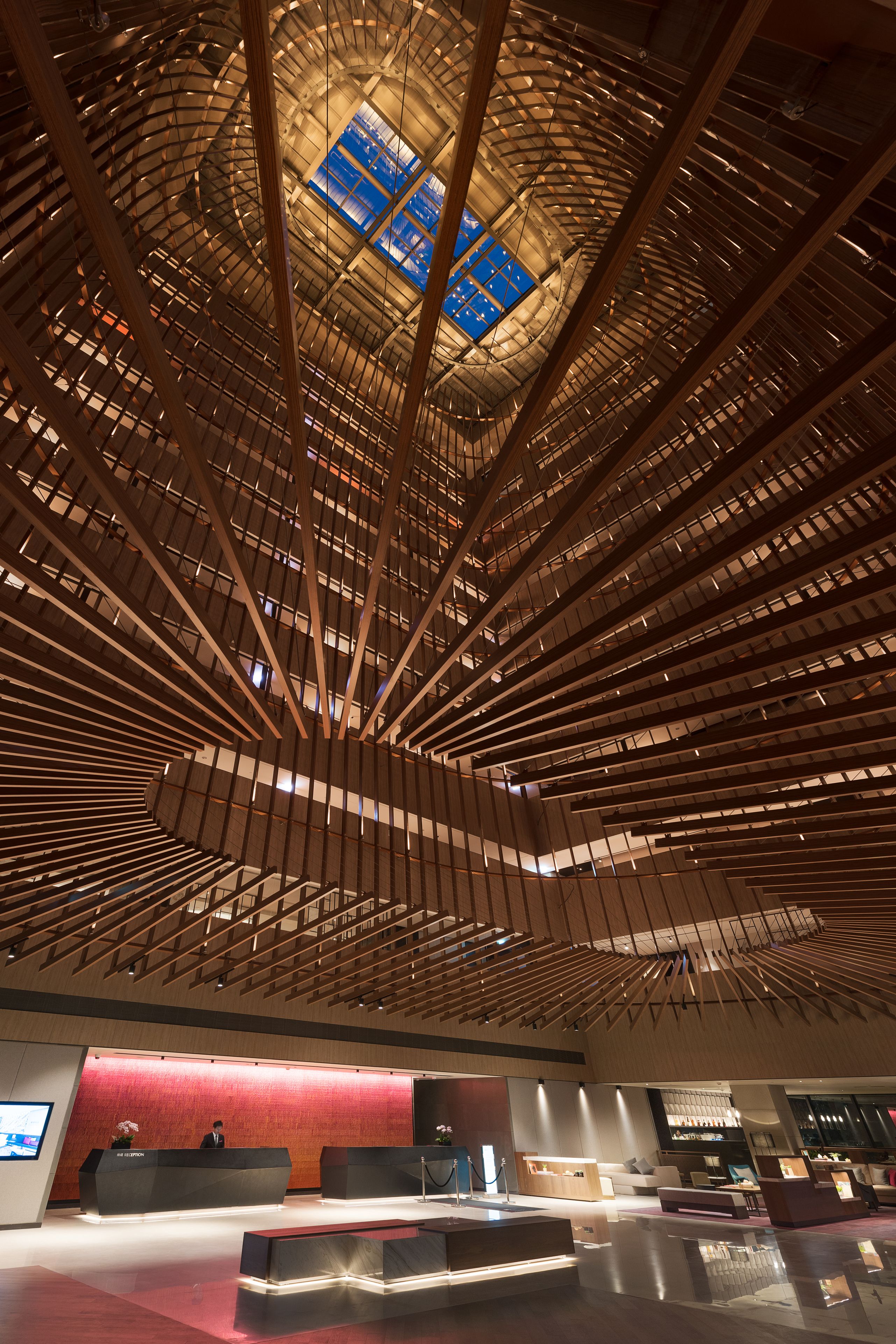 Un vestíbulo moderno con un diseño único de techo de madera, un mostrador de recepción y una gran pantalla digital.