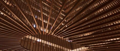 A modern lobby with a unique wooden ceiling design, a reception desk, and a large digital screen.