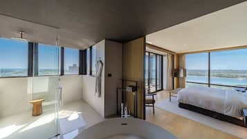 A modern hotel room with a large bed, a bathtub, and a view of the city.