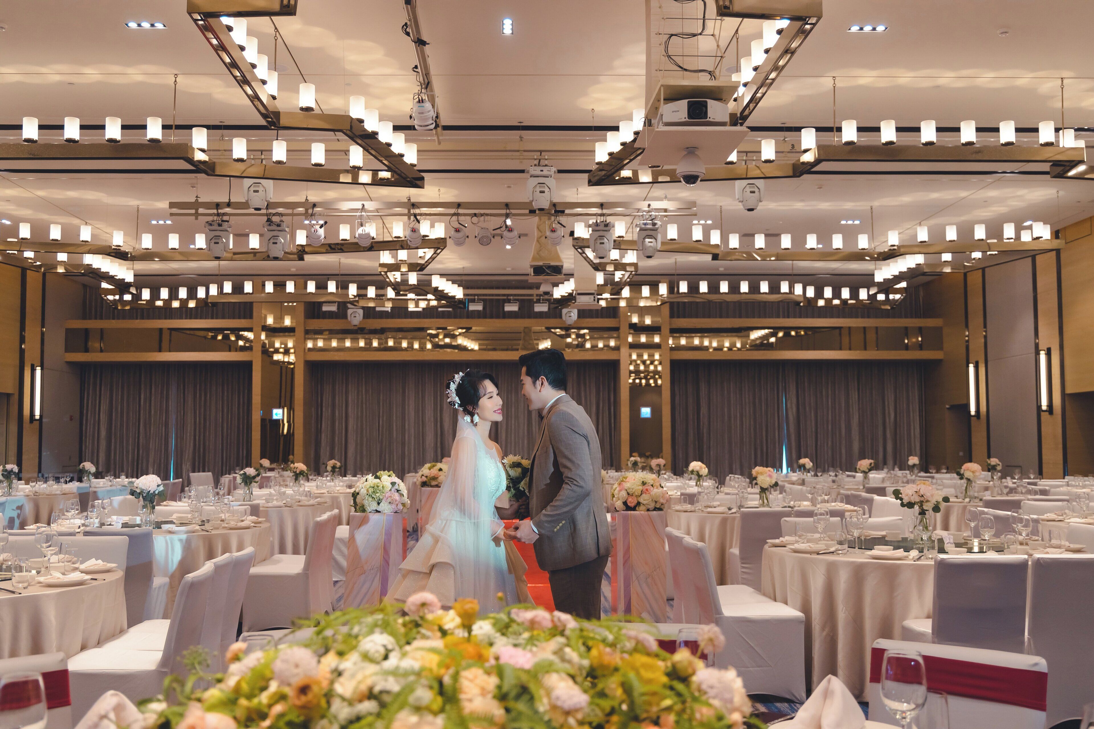 A banquet hall with round tables, white tablecloths, and floral centerpieces.