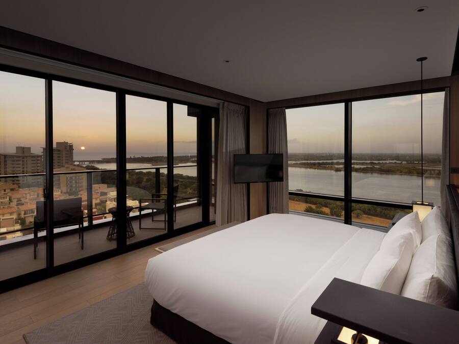 Una habitación de hotel moderna con una cama grande, un televisor y un balcón con vista a la ciudad.