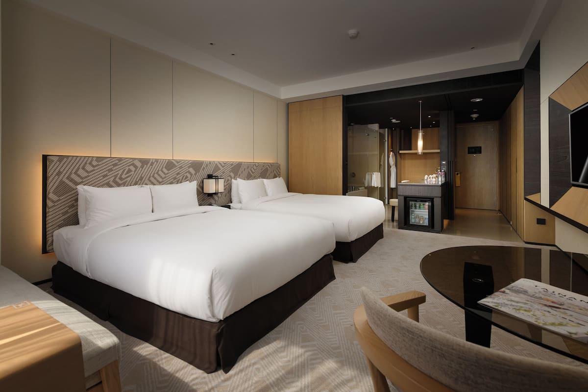 A hotel room with two beds, a small table, and a seating area.