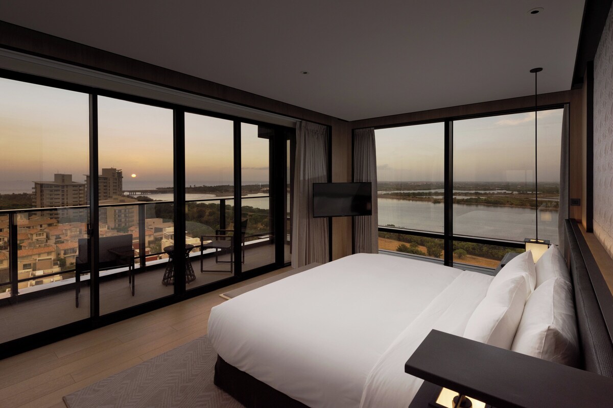 A modern hotel room with a large bed, a TV, and a balcony with a city view.