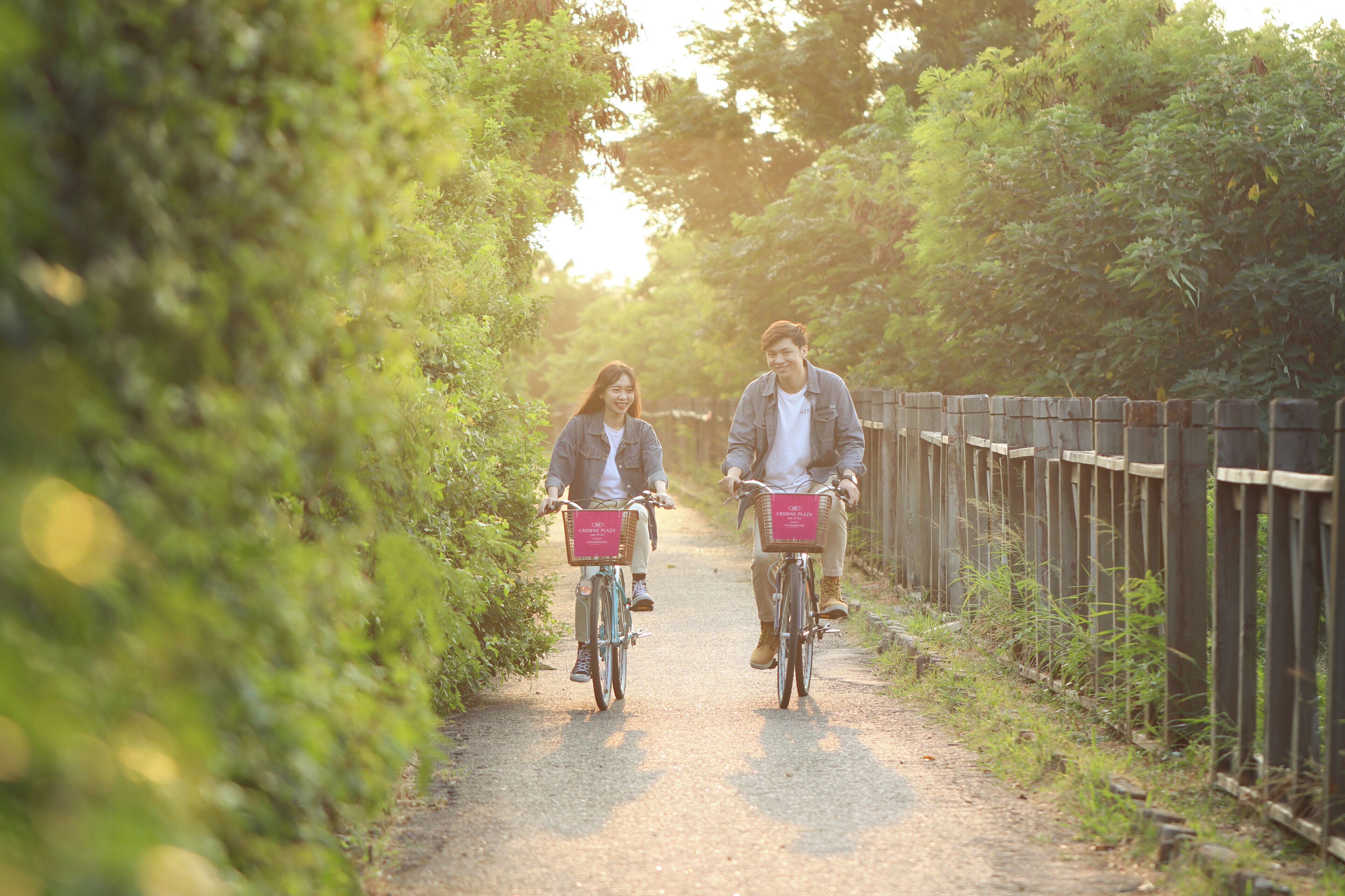 Two people riding bicycles on a gravel path surrounded by greenery.