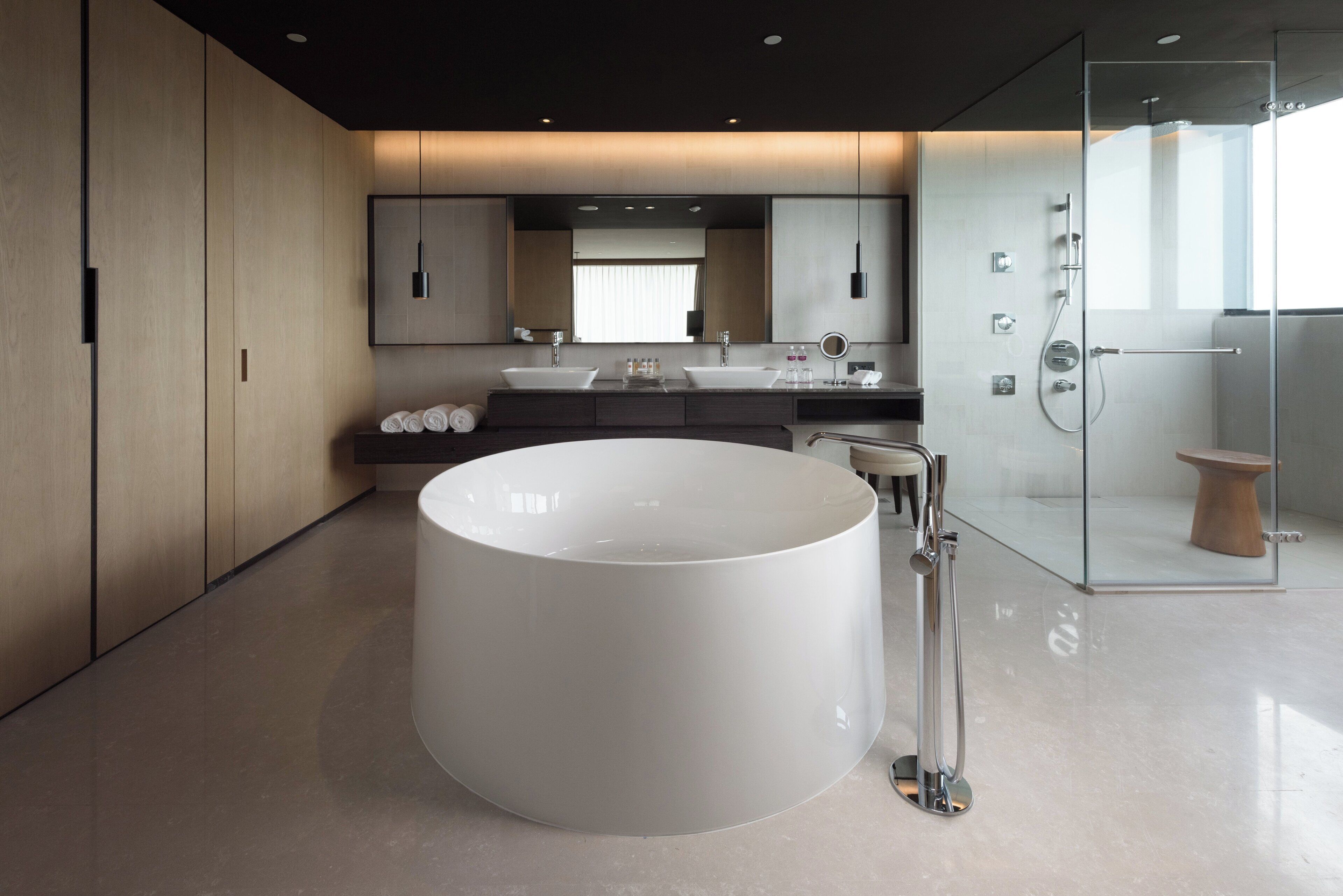A modern bathroom with a large central sink, a glass-enclosed shower, and a large mirror above the sink.