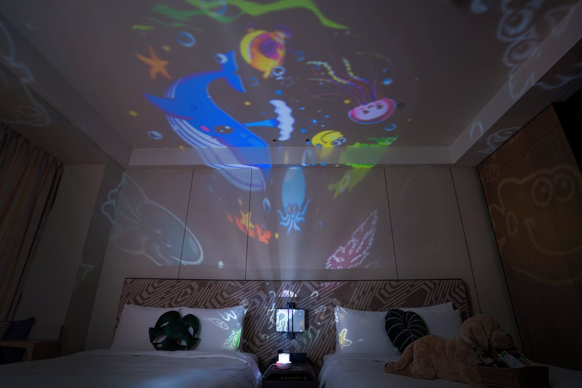 A hotel room with a bed, a television, and a ceiling projection of a colorful underwater scene.