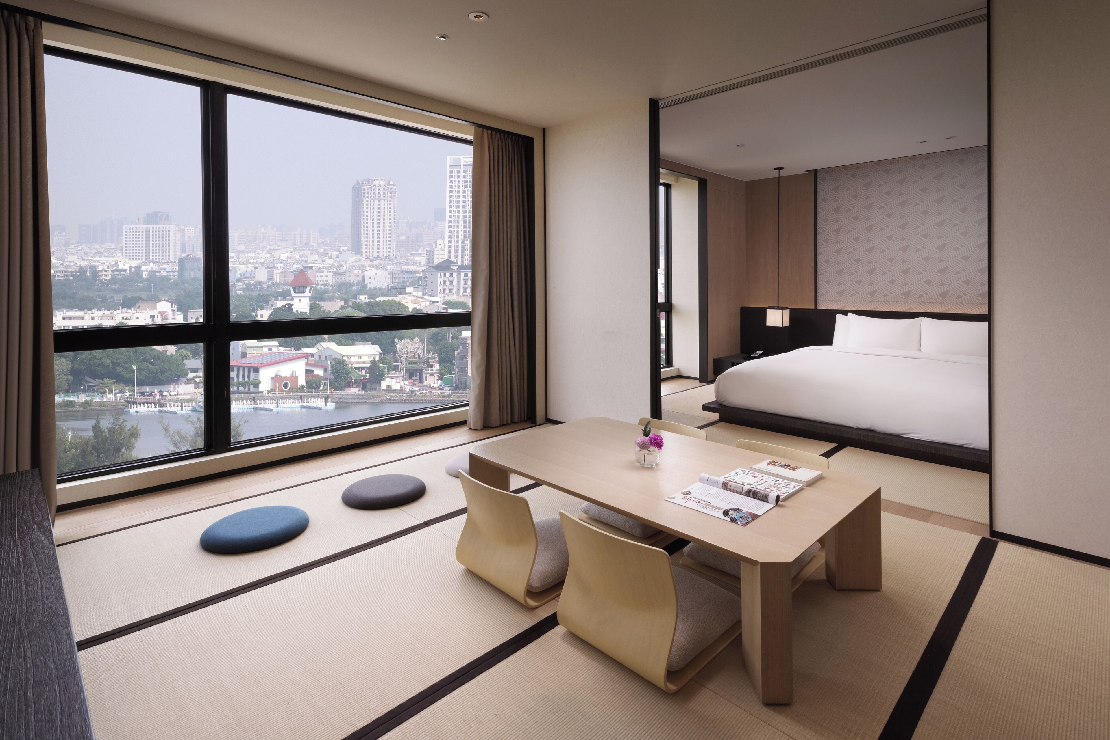 A hotel room with a large window, a bed, a table with chairs, and tatami mats.