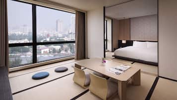 A hotel room with a large window, a bed, a table with chairs, and tatami mats.