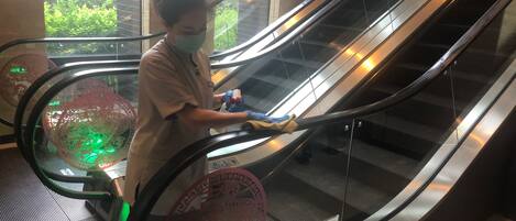 An escalator with a person standing on it, wearing a mask and gloves, holding a cleaning cloth.