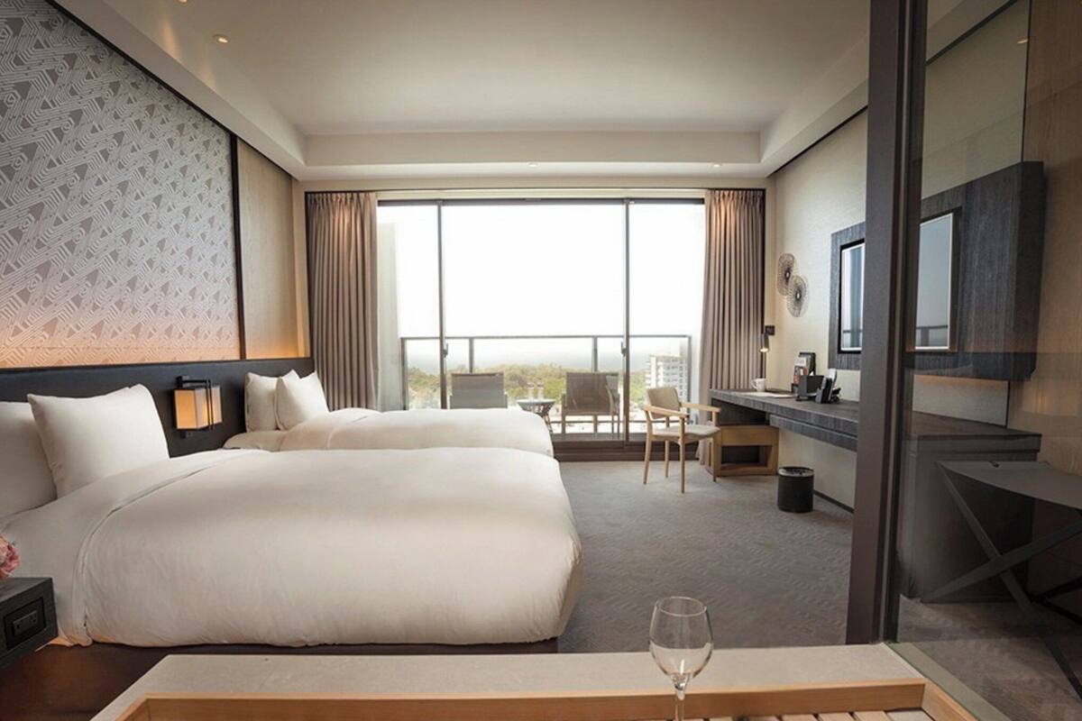A hotel room with a large bed, a desk, a chair, a TV, and a balcony with a view.
