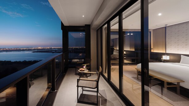 Habitación de hotel moderna con balcón y vista a la ciudad al atardecer.