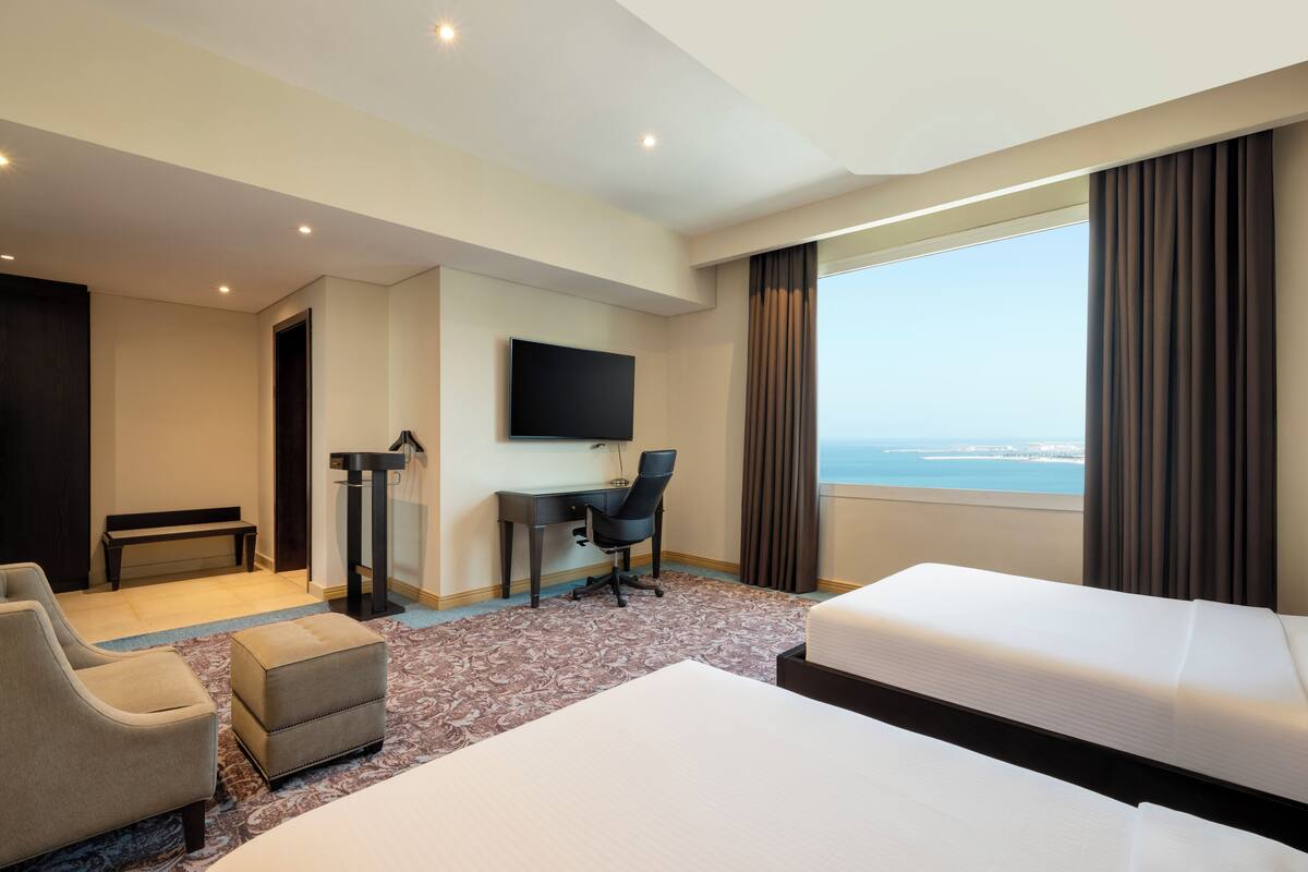 Une chambre d’hôtel avec un lit, un bureau, une chaise, une télévision et une vue sur la mer.