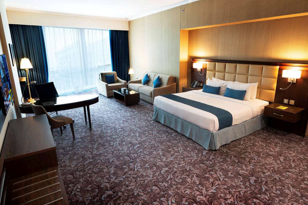 Une chambre d’hôtel avec un grand lit, deux fauteuils, un bureau avec un ordinateur et une télévision.