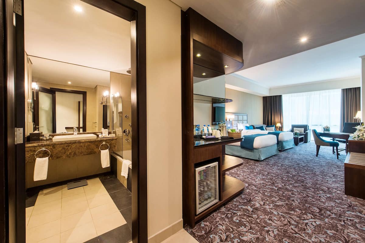 Une chambre d’hôtel avec salle de bain, un espace de vie comprenant un canapé et une table à manger, ainsi qu’un grand miroir.