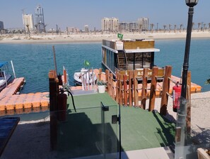 Een kade aan het water met een houten constructie, een boot en een stadsgezicht op de achtergrond.