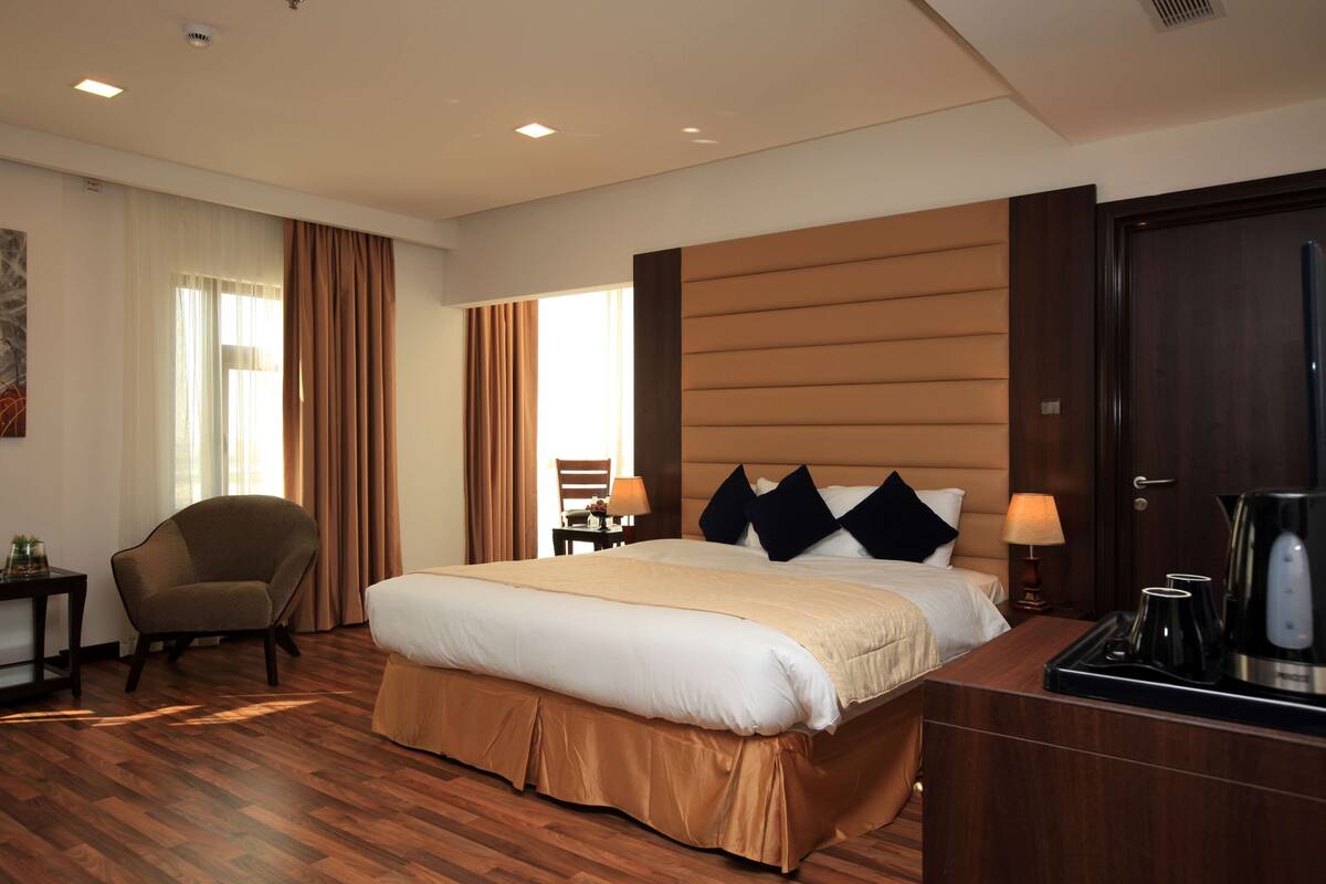 Ein Hotelzimmer mit einem großen Bett, einem Sessel, einem Schreibtisch mit Lampe und einer Kaffeemaschine.