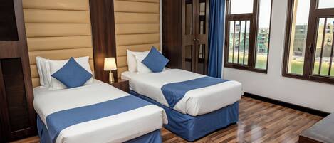 A hotel room with two beds, wooden flooring, a large window, and a view of the outside.