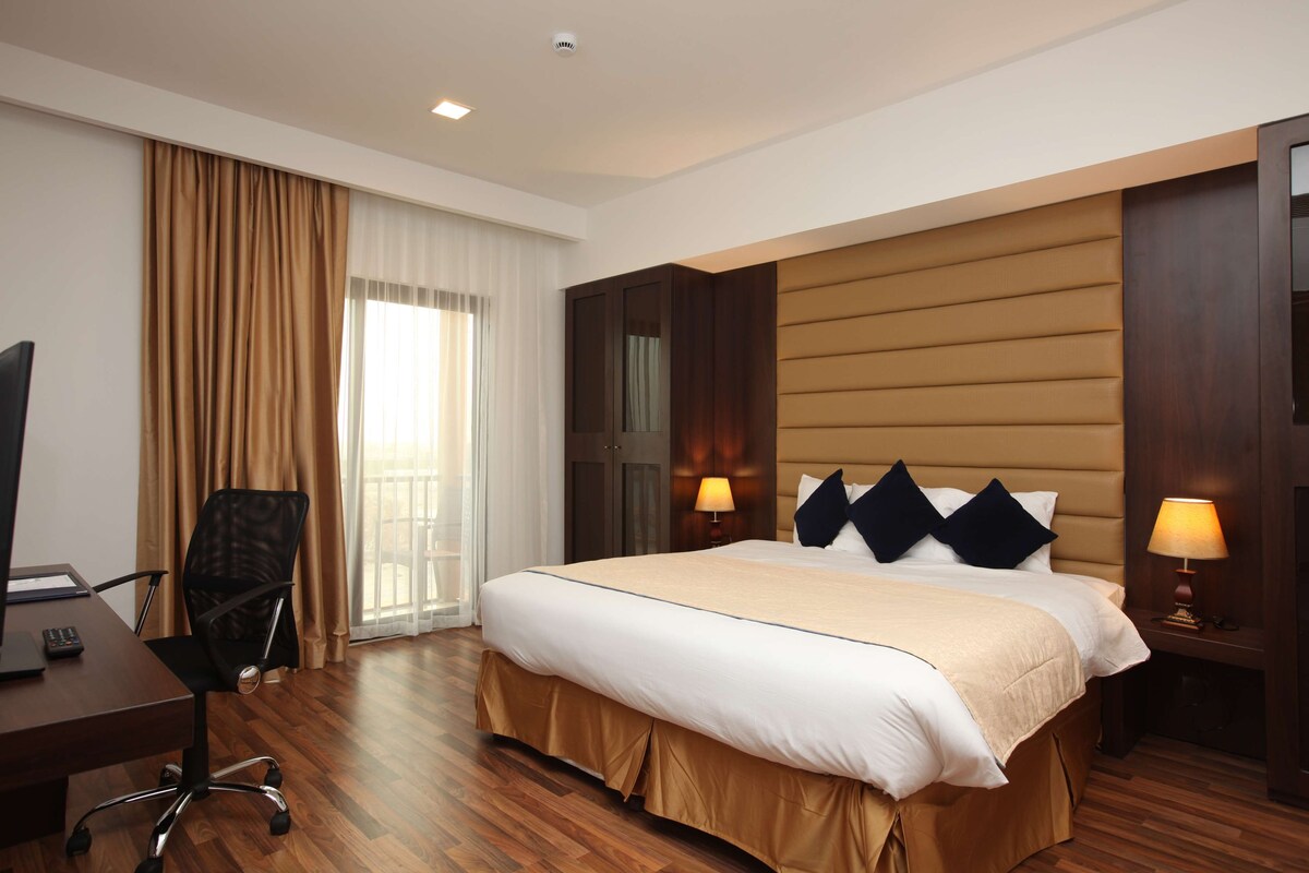 A hotel room with a large bed, a desk with a chair, a television, and a window with curtains.