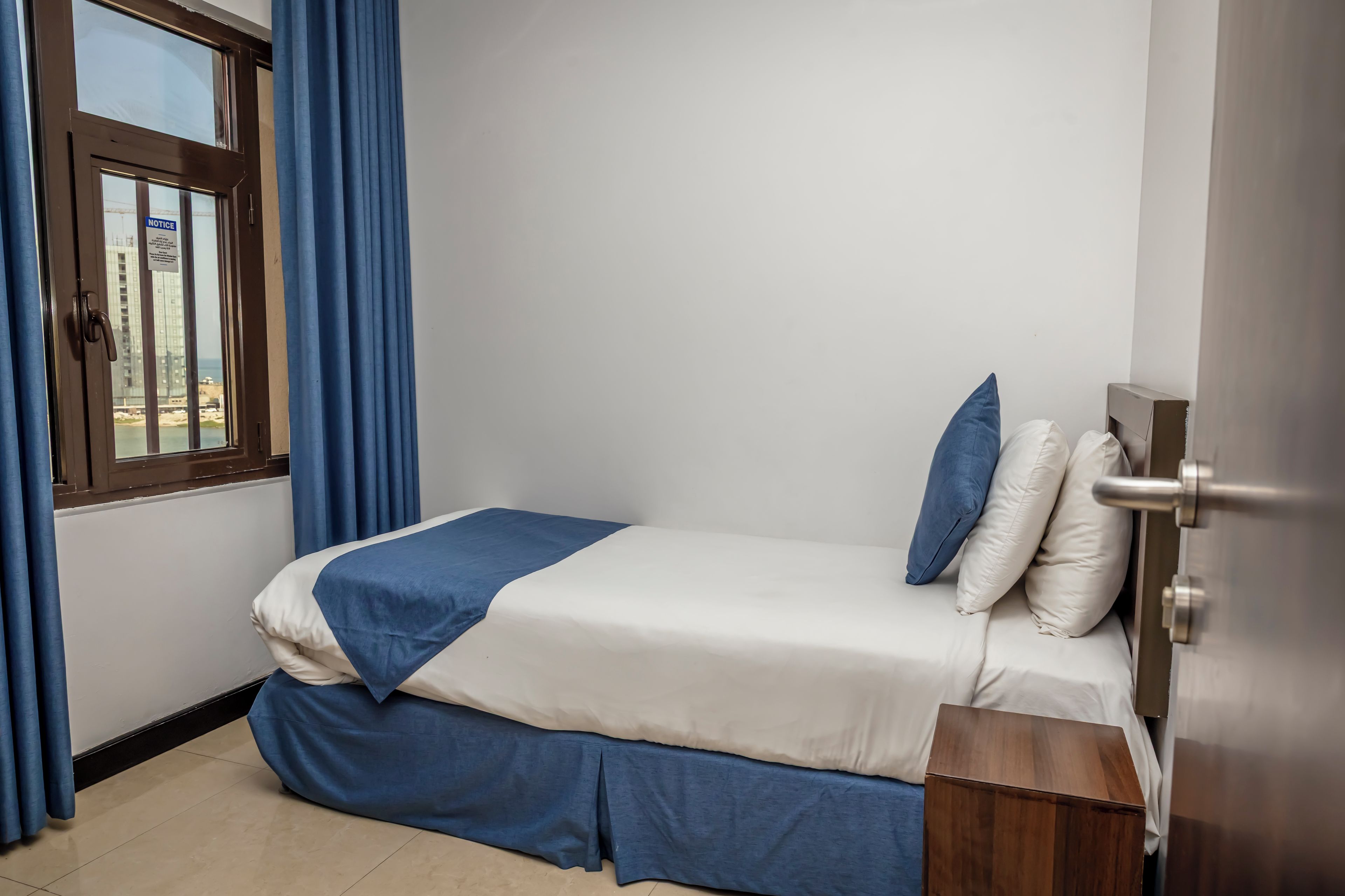 A single bed with a blue and white bedspread, two pillows, and a wooden nightstand.