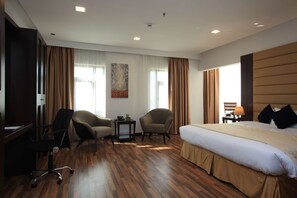 A hotel room with a large bed, two armchairs, a desk, and a small table. - Golden Tulip Al Khobar Suites (Al Khobar)