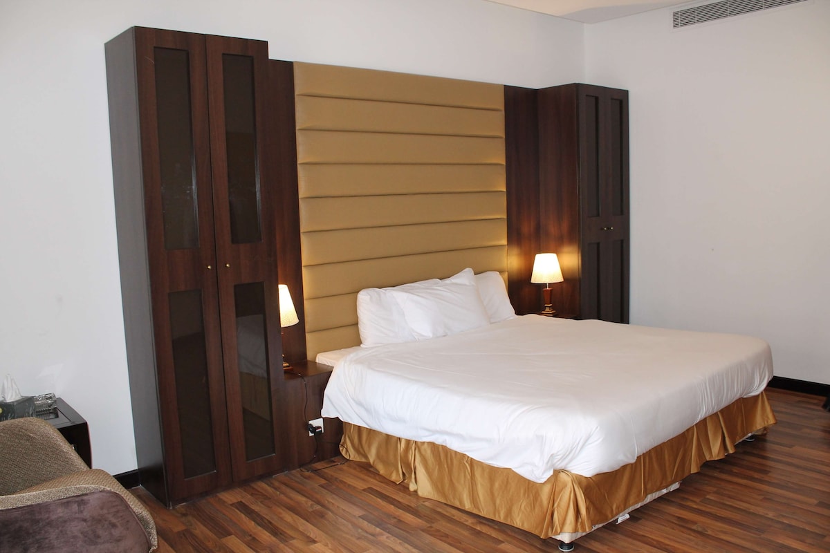 A hotel room with a large bed, wooden flooring, a wardrobe with glass doors, and bedside lamps.