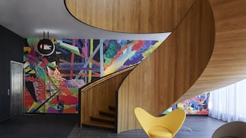 A modern interior with a curved wooden staircase, colorful abstract wall art, and a seating area with vibrant chairs.