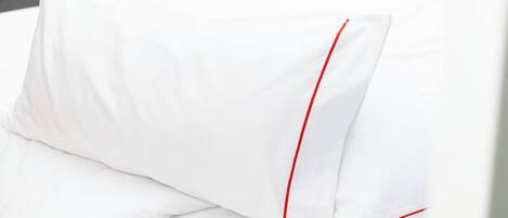 Almohada blanca con costuras rojas sobre una cama.