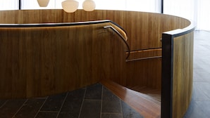 A modern interior with a curved wooden reception desk, a black metal handrail, and multiple hanging pendant lights with a ribbed design. - citizenM London Shoreditch (London)