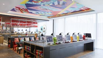 Un área de bar moderna con un mural en el techo, una barra larga con varios monitores y una estantería llena de libros.