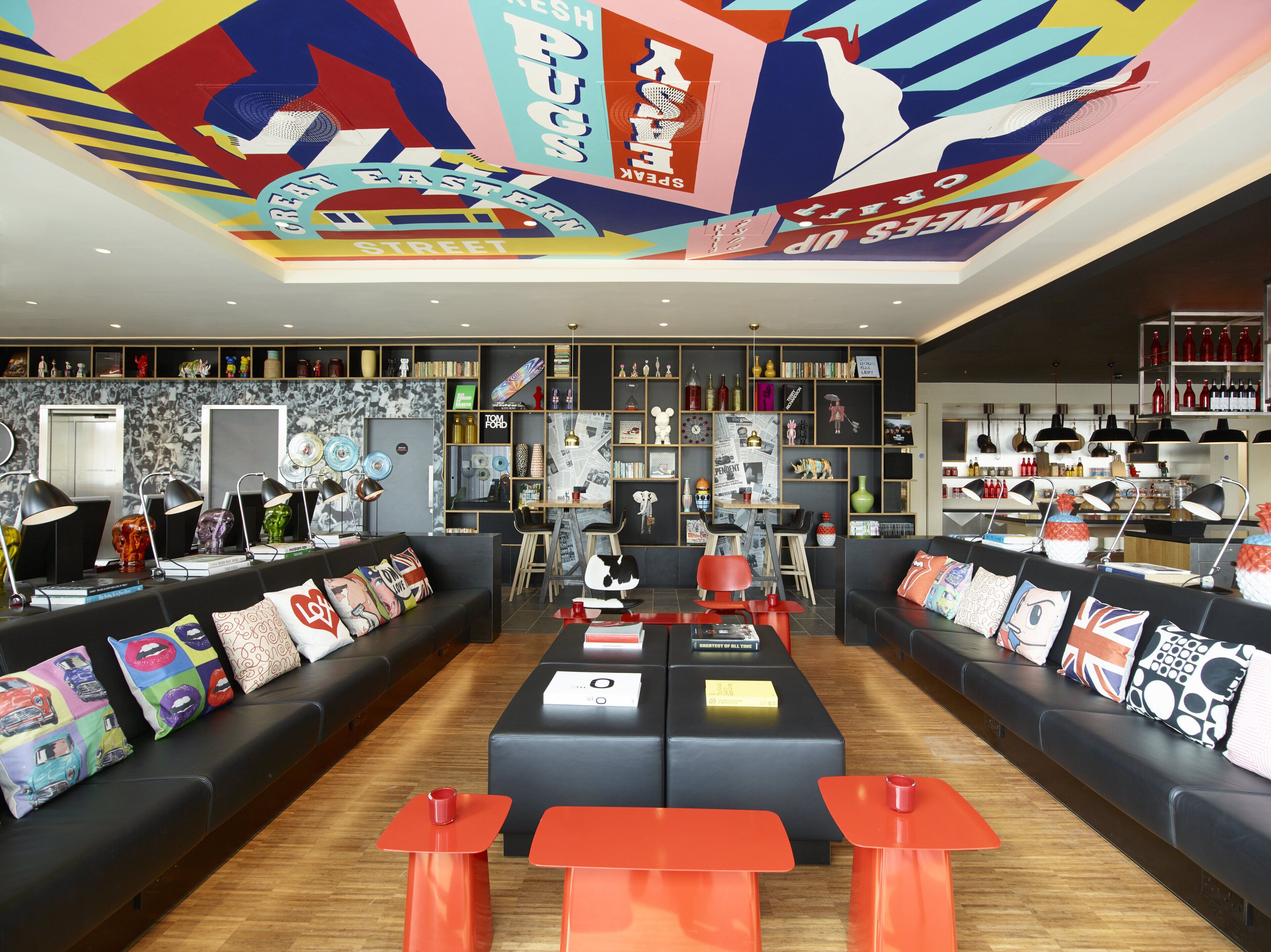 A modern lounge area with black sofas, red tables, and a ceiling mural.