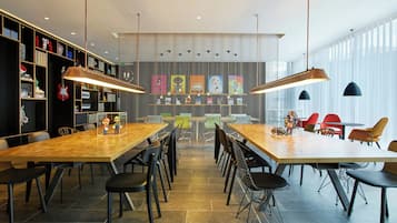 Un'area pranzo moderna con un lungo tavolo in legno e sedie nere, circondata da scaffali e opere d'arte alle pareti.