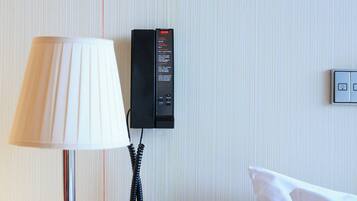 A hotel room with a round table, a lamp, a telephone, and a bed.
