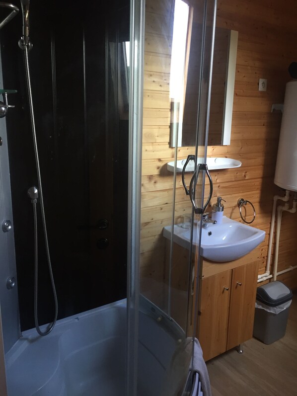 A bathroom with a glass-enclosed shower, a sink, and wooden walls. - Le Petit Robinson (Champvert)