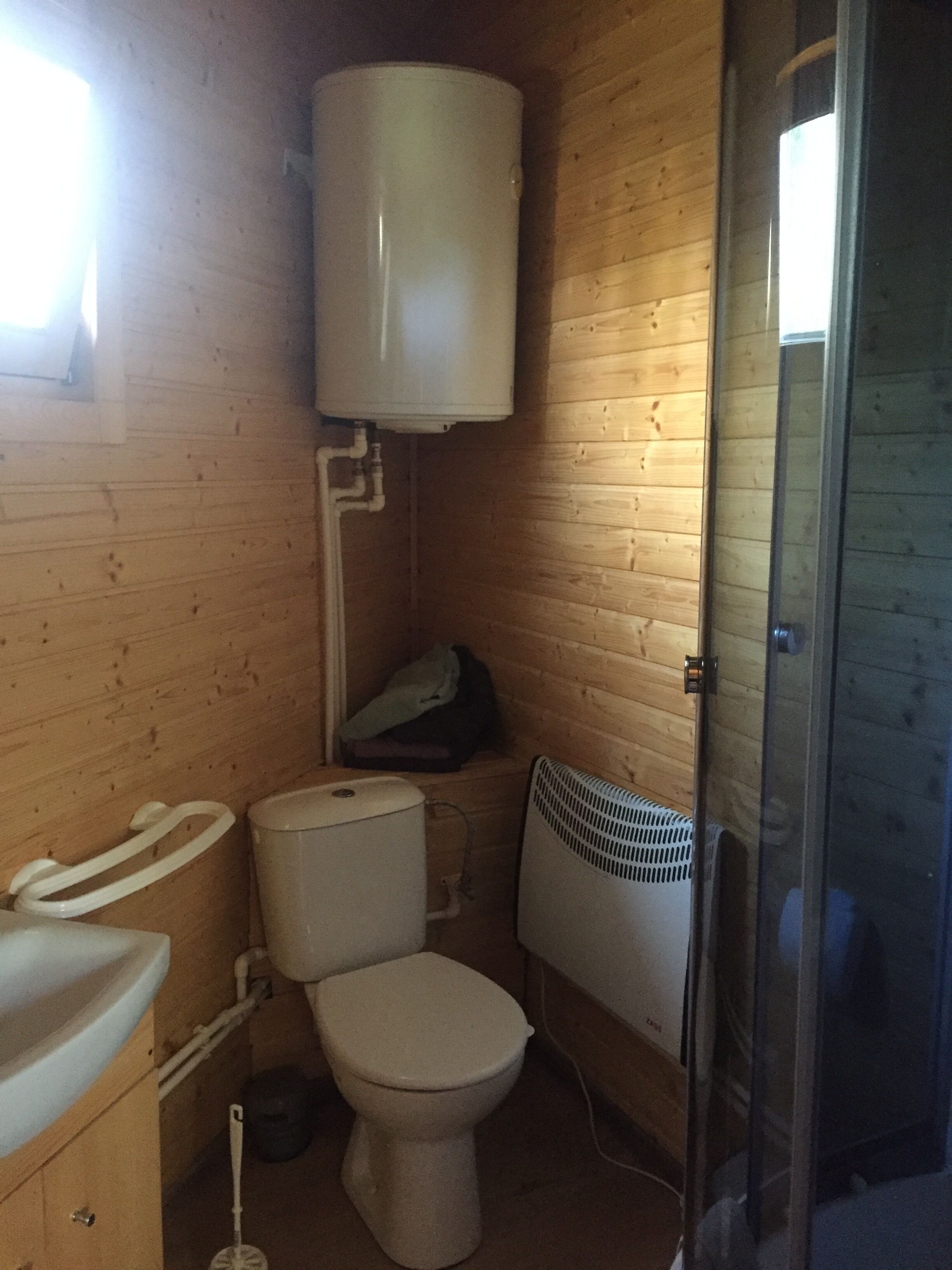 A compact wooden bathroom with a toilet, sink, and a radiator.