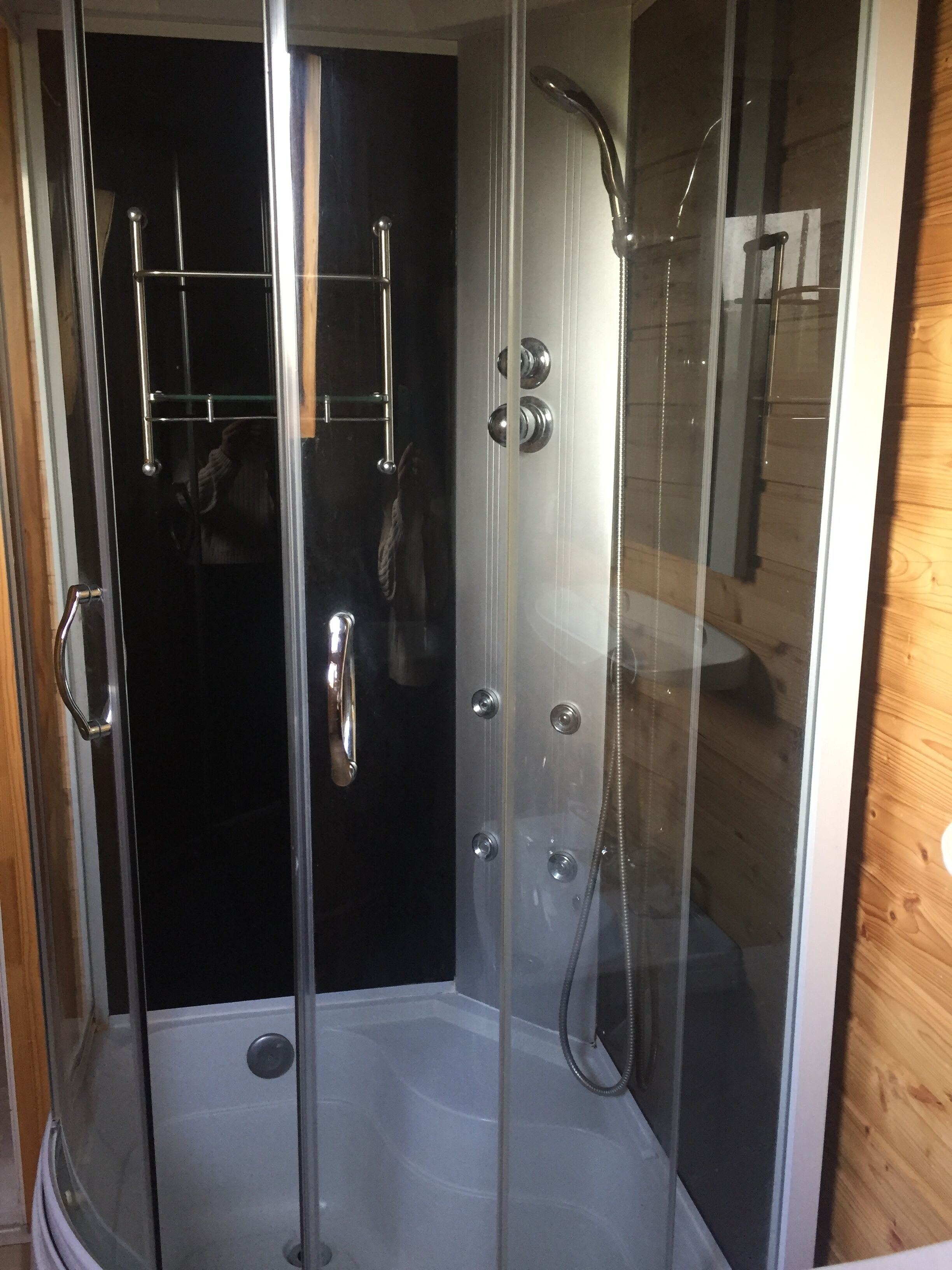 A glass-enclosed shower stall with a handheld showerhead and a handheld faucet.