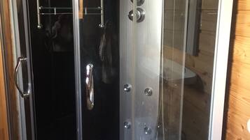 A glass-enclosed shower stall with a handheld showerhead and a handheld faucet.