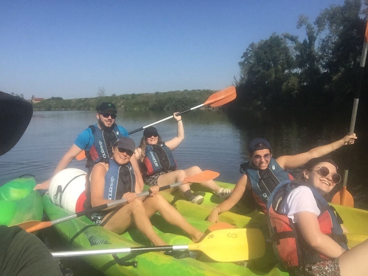Eine Gruppe von Menschen in einem grünen Kanu auf ruhigem Wasser.