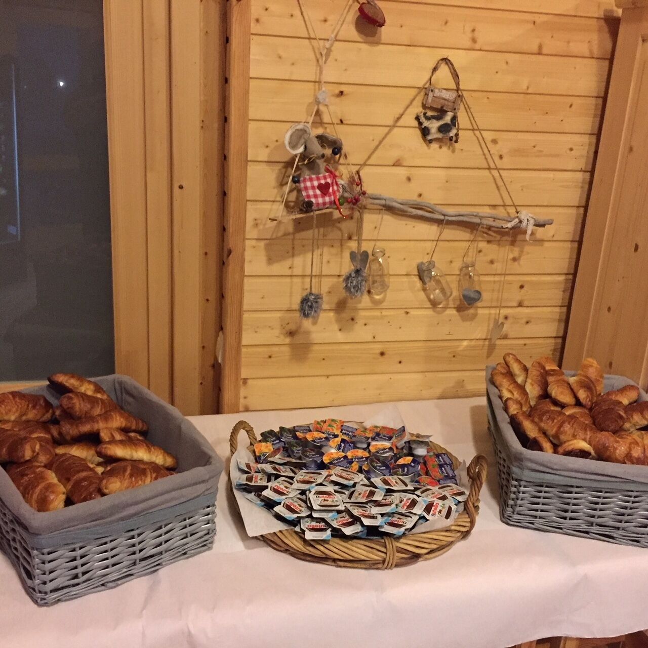 Ett bord med korgar fulla av bakverk och choklad, en trävägg med upphängda dekorationer och ett fönster i bakgrunden.