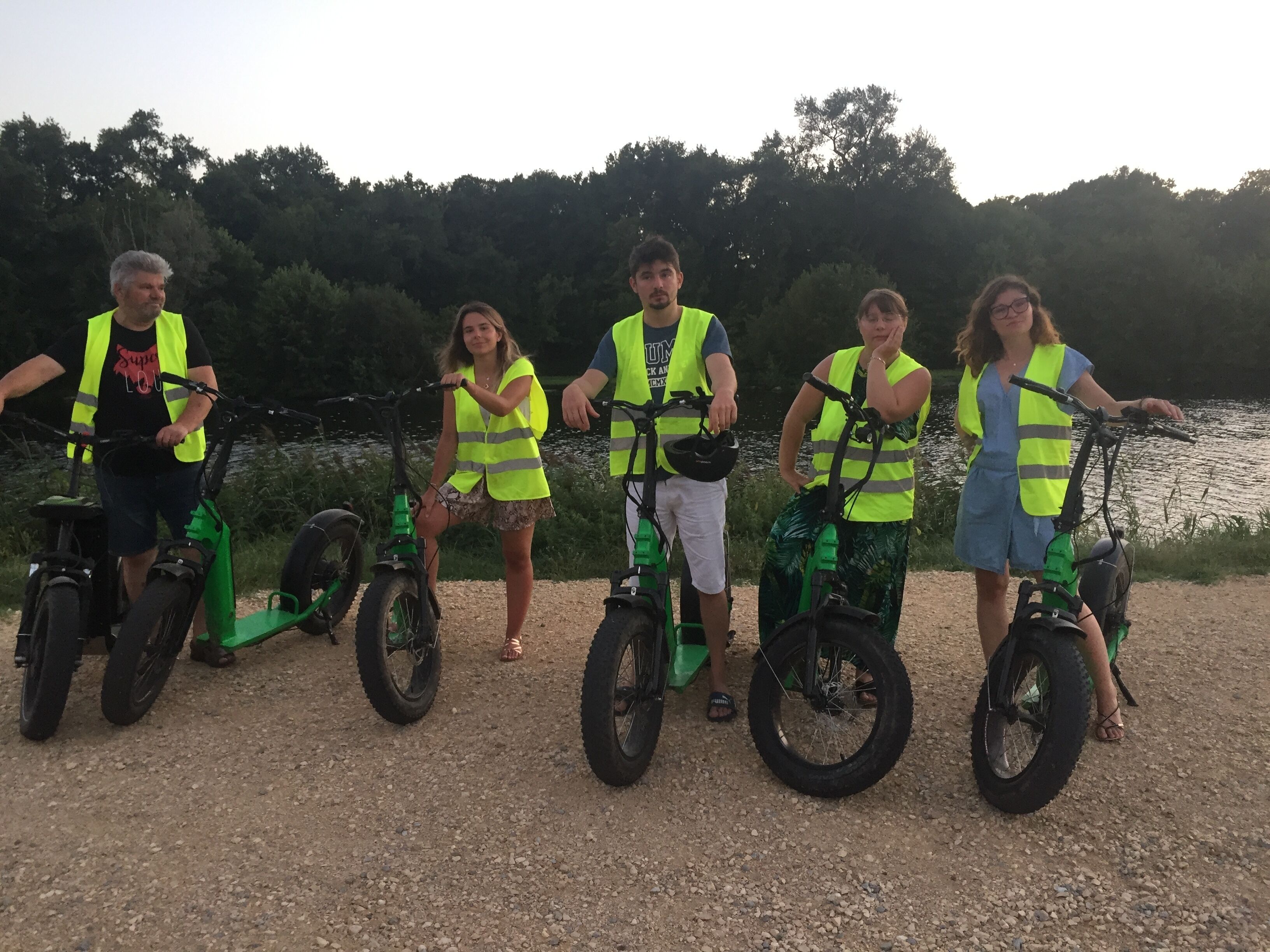 En grupp människor på elcyklar, nära ett vattendrag.