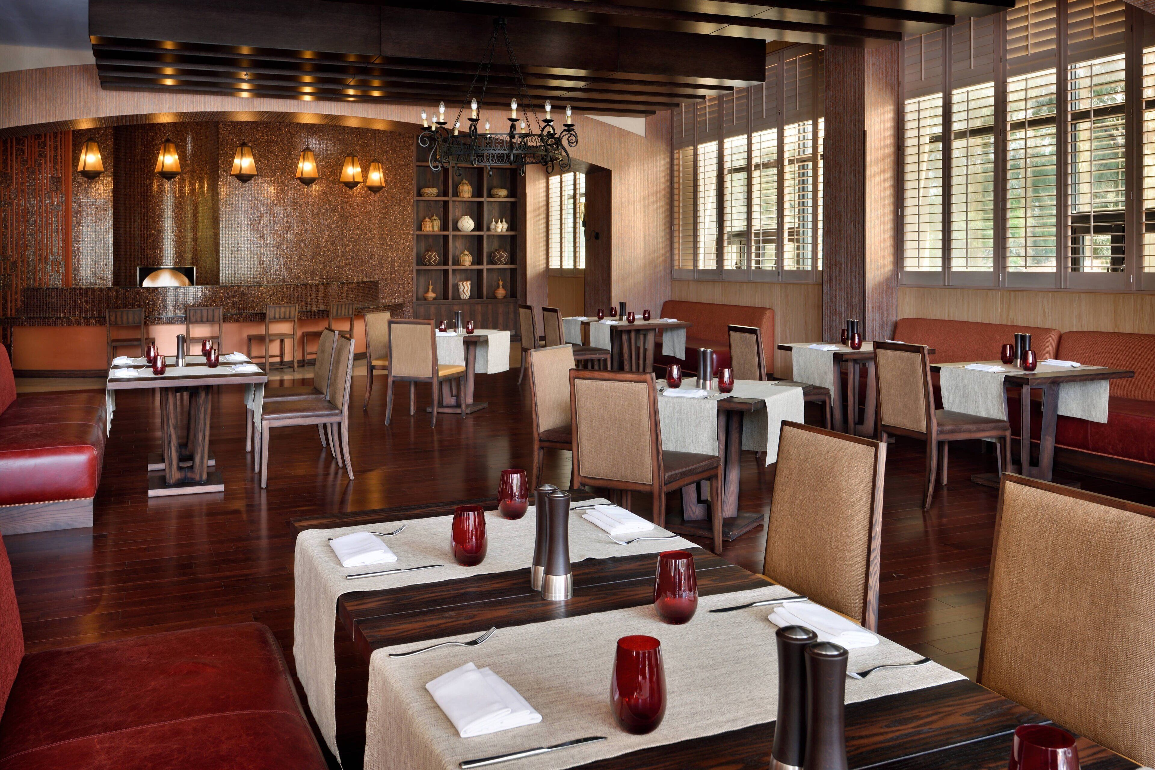 A restaurant with multiple dining tables, chairs, and a bar area with shelves of bottles.
