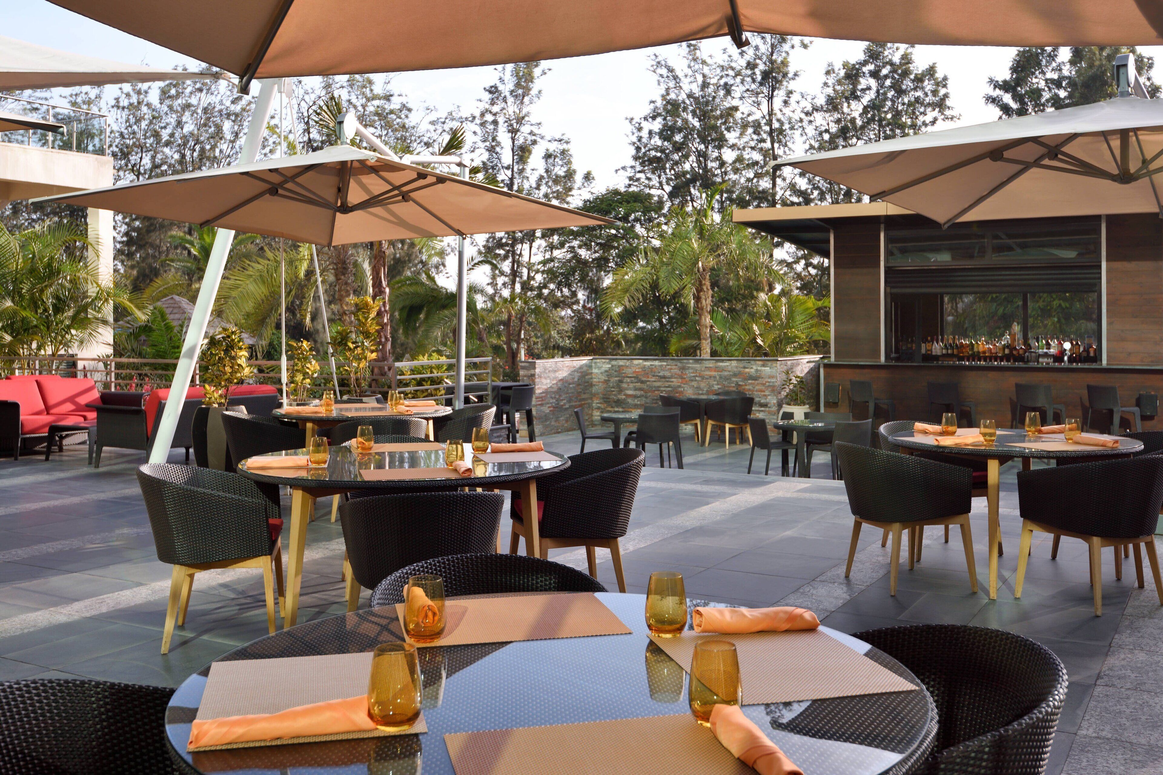 An outdoor dining area with round tables, black wicker chairs, and beige umbrellas.