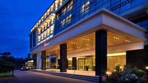 Un hotel moderno con fachada de vidrio, acceso cubierto y zona exterior ajardinada.