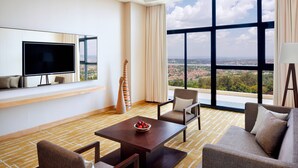 Un hotel moderno con una ventana grande que ofrece vistas a la ciudad, un televisor de pantalla plana, una mesa de comedor con frutero y un sofá.