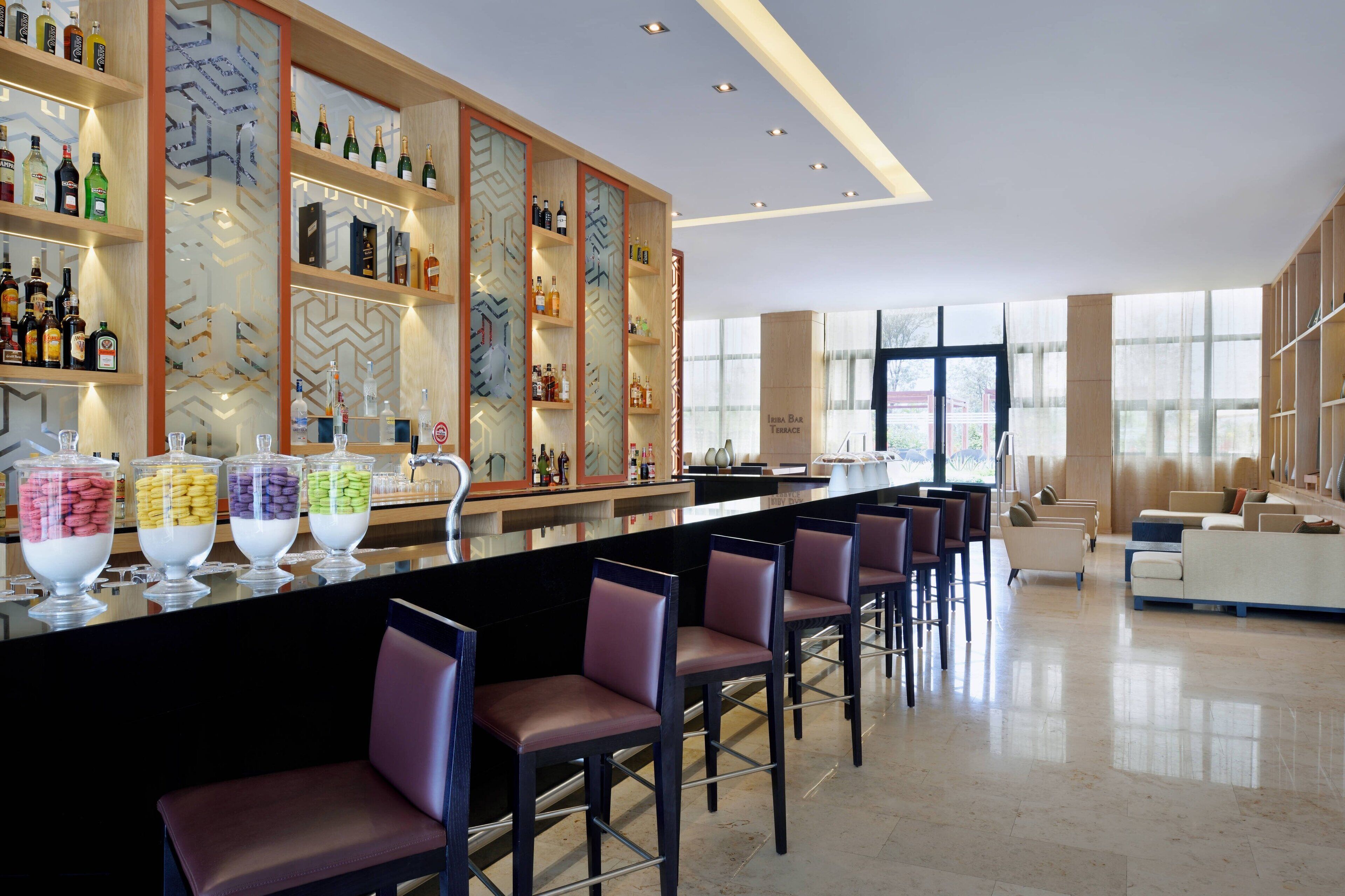 A bar area with multiple seating options, a variety of liquor bottles on shelves, and a clear view of the outside through large windows.