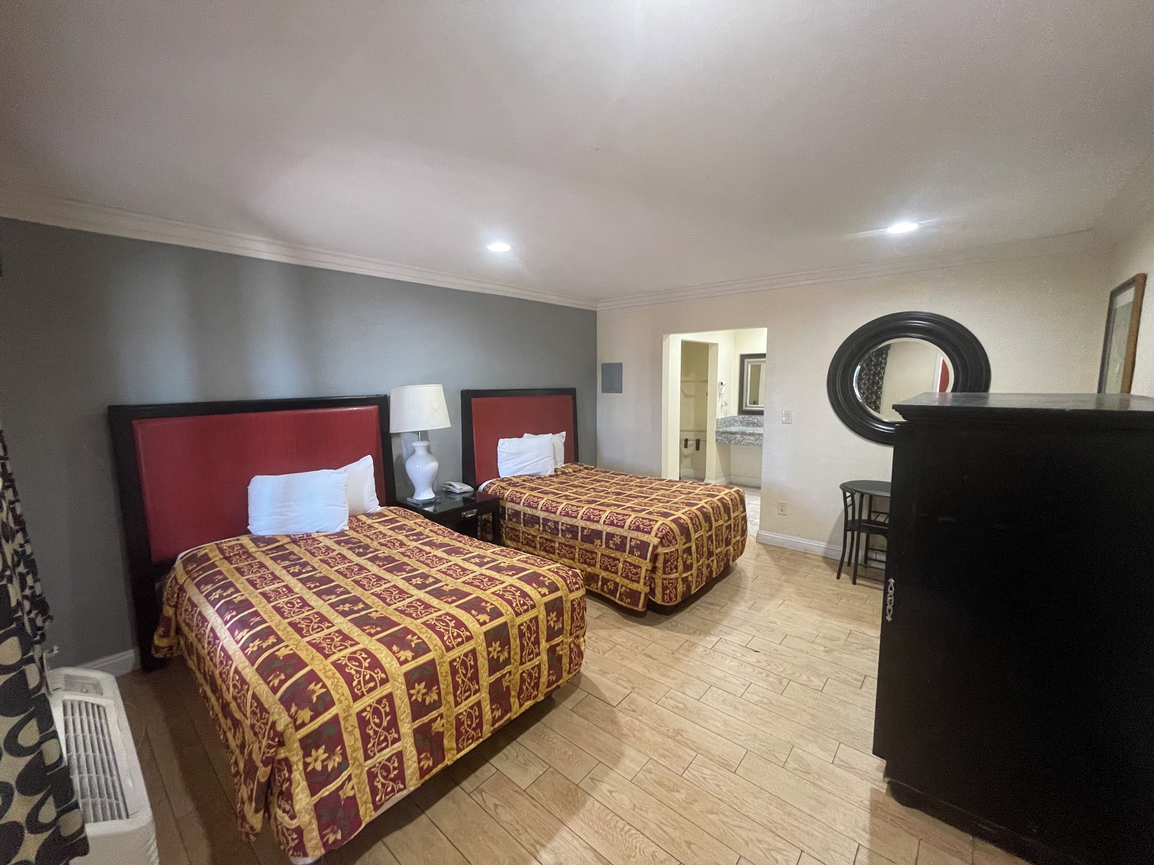 A hotel room with two beds, a desk, a chair, a mirror, and a refrigerator.