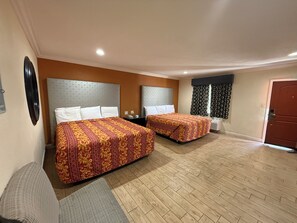 A hotel room with two beds, a sofa, a desk, and a window with curtains.