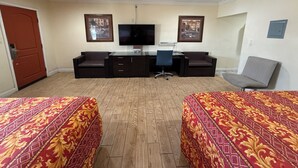 Une chambre d’hôtel avec deux lits, un bureau, une chaise, une télévision et deux tableaux encadrés au mur.