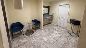 Une salle de bain avec un lavabo, un miroir et une porte. On y trouve deux chaises et une petite table.