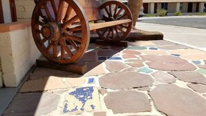 Un chariot en bois, doté de grandes roues, est placé sur un sol carrelé, avec un mur de pierre en arrière-plan.